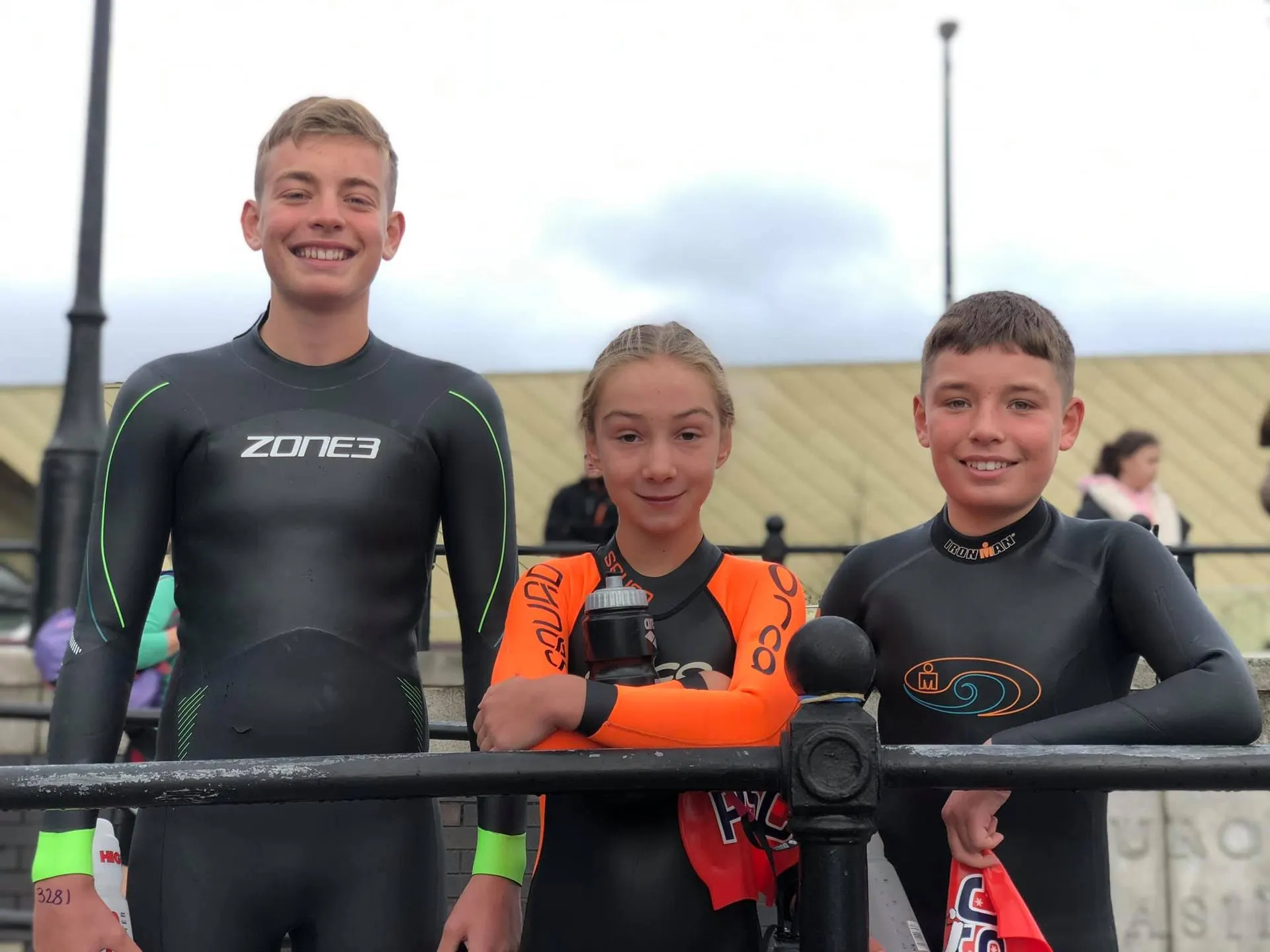 Three junior triathletes in wetsuits smiling before a race